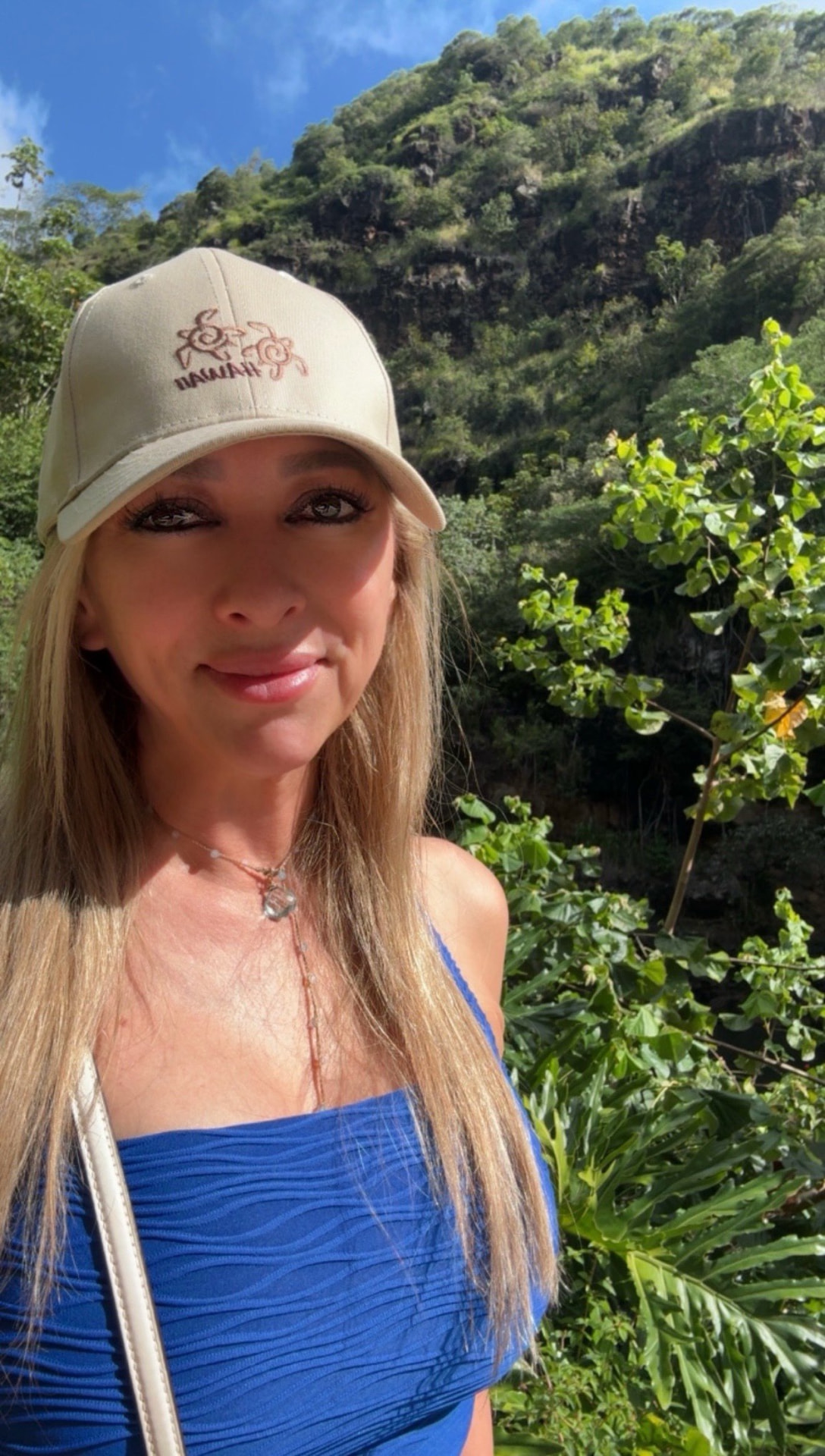 Sabrina Vargas outdoors on a hike, wearing a Hawaii cap, in front of a green mountainside.